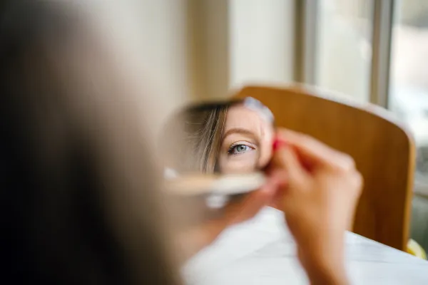 A woman looking through a mirror, with her eyes showing in the reflection.