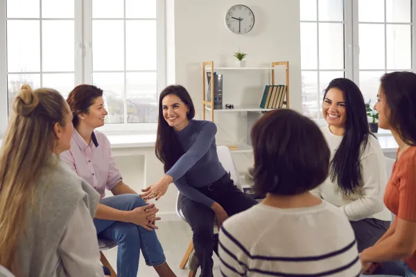 A photo of a group of women in a circle, discussion and smiling with each other.