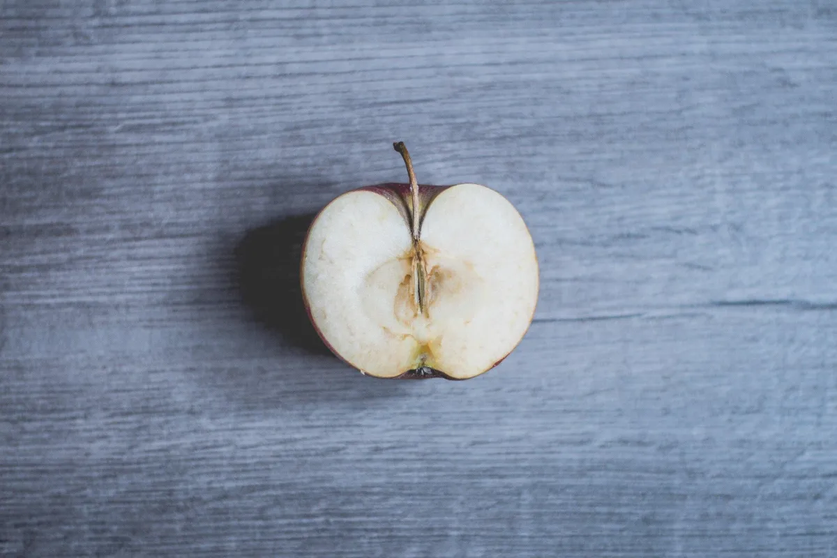 Apple cut in half to see core. Apple is placed on gray wood table.
