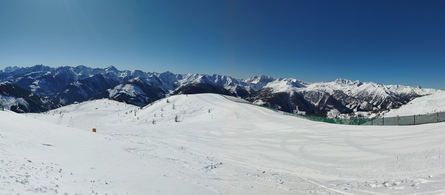 Weites Panorama einer frisch präparierten Skipiste am Golzentipp in Obertilliach unter strahlend blauem Himmel mit Blick auf die verschneiten Alpengipfel