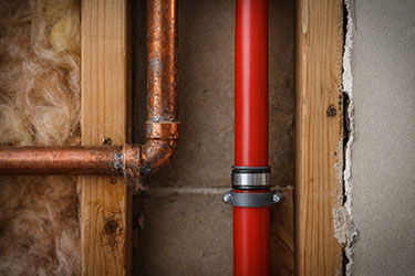 Exposed pipes on wood framing behind a sheetrock wall.