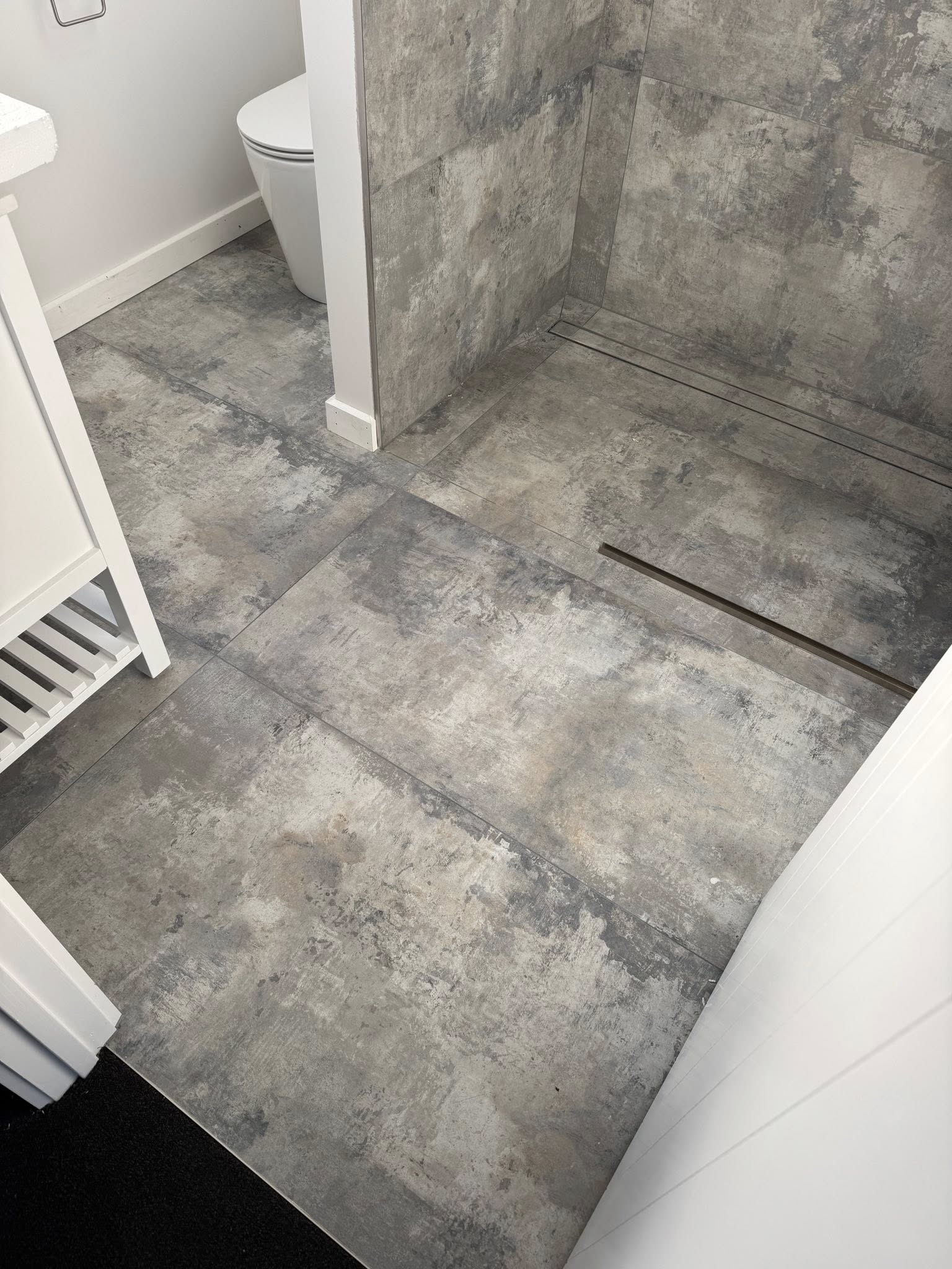 Large format dark grey floor tiles with linear drain installed in a residential bathroom by Remarkable Contracting in Hawke's Bay