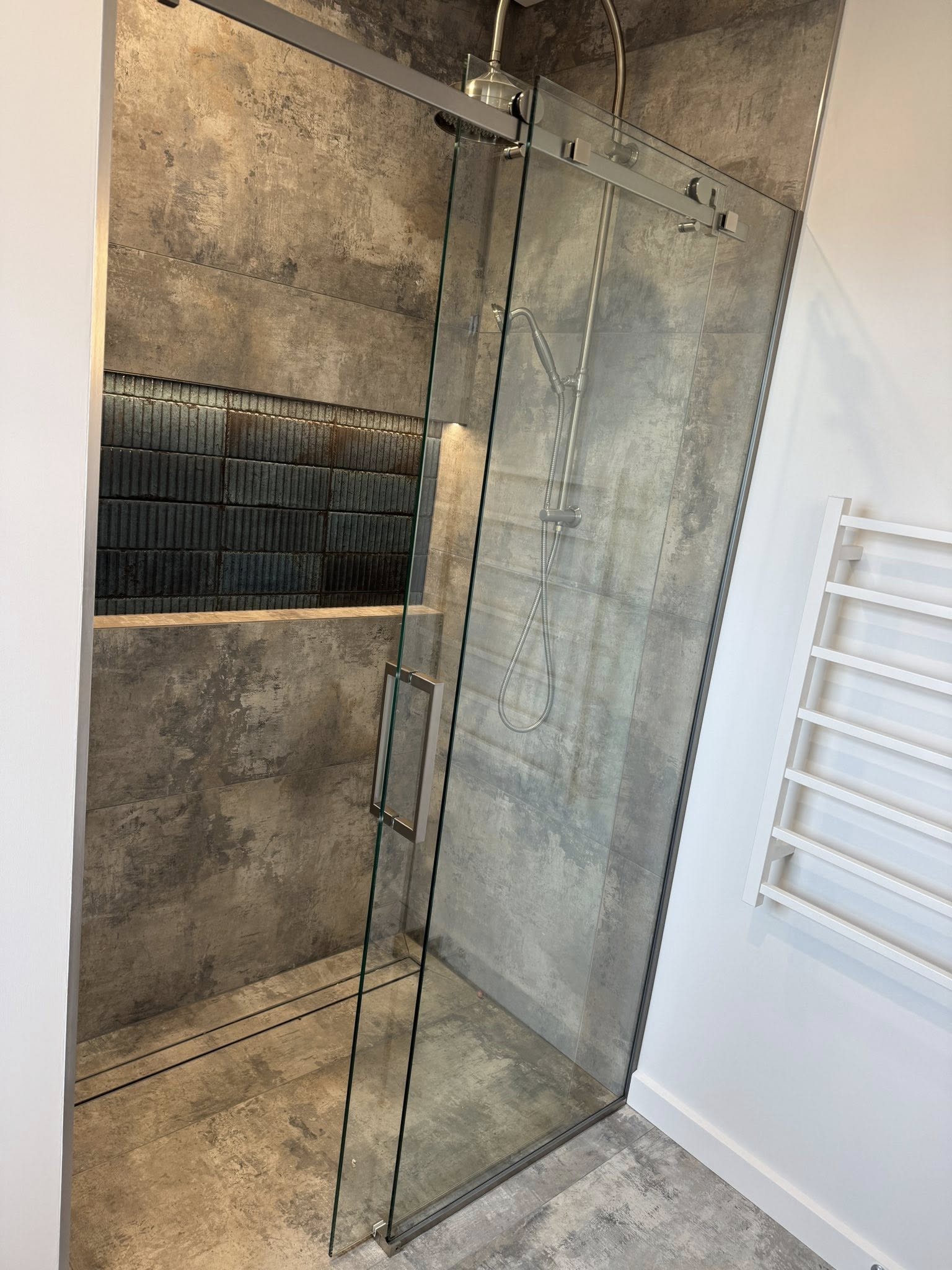 Corner shower renovation with dark feature wall tiling and frameless glass door by Remarkable Contracting in Hawke's Bay