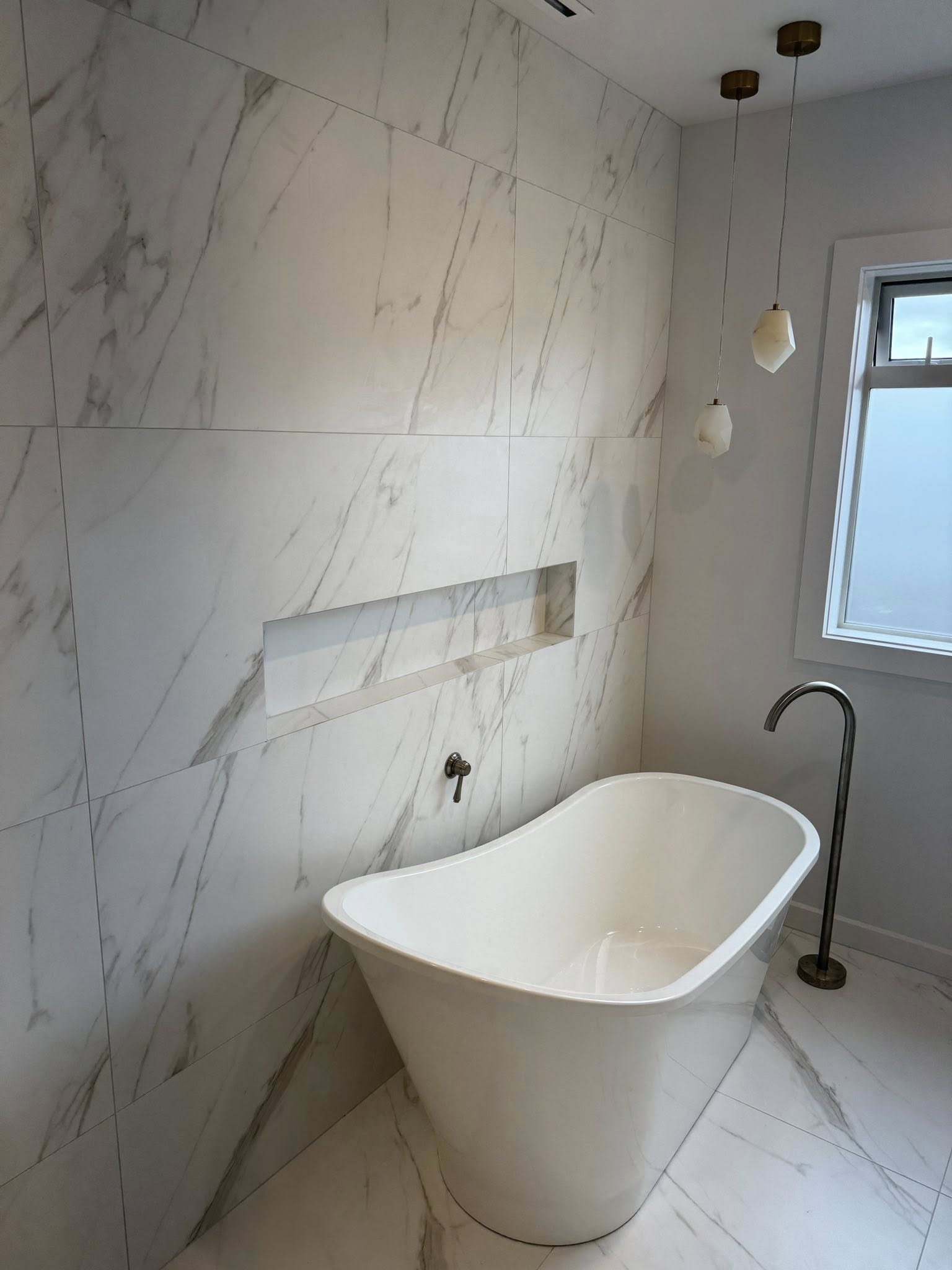 Freestanding bath set against full height marble look wall tiling completed by Remarkable Contracting in Hawke's Bay