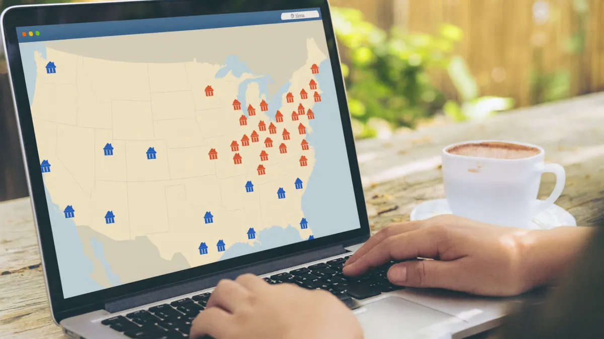 Person using a laptop outdoors with a map of the United States on the screen, showing red and blue icons representing different locations across the country. A cup of coffee sits on the wooden table next to the laptop