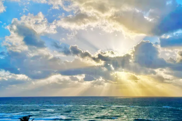 unlight breaking through clouds over the ocean, symbolizing the infinite and transcendent nature of Divine Love beyond creation.