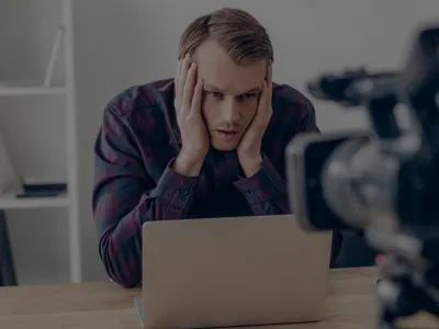 Business owner in Newnan GA experiencing camera anxiety during video recording, sitting at a desk with a laptop and camera.