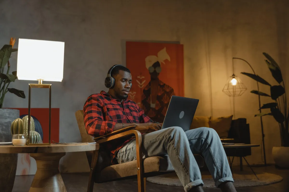 Man sitting in chair at home working on laptop with headphones on.