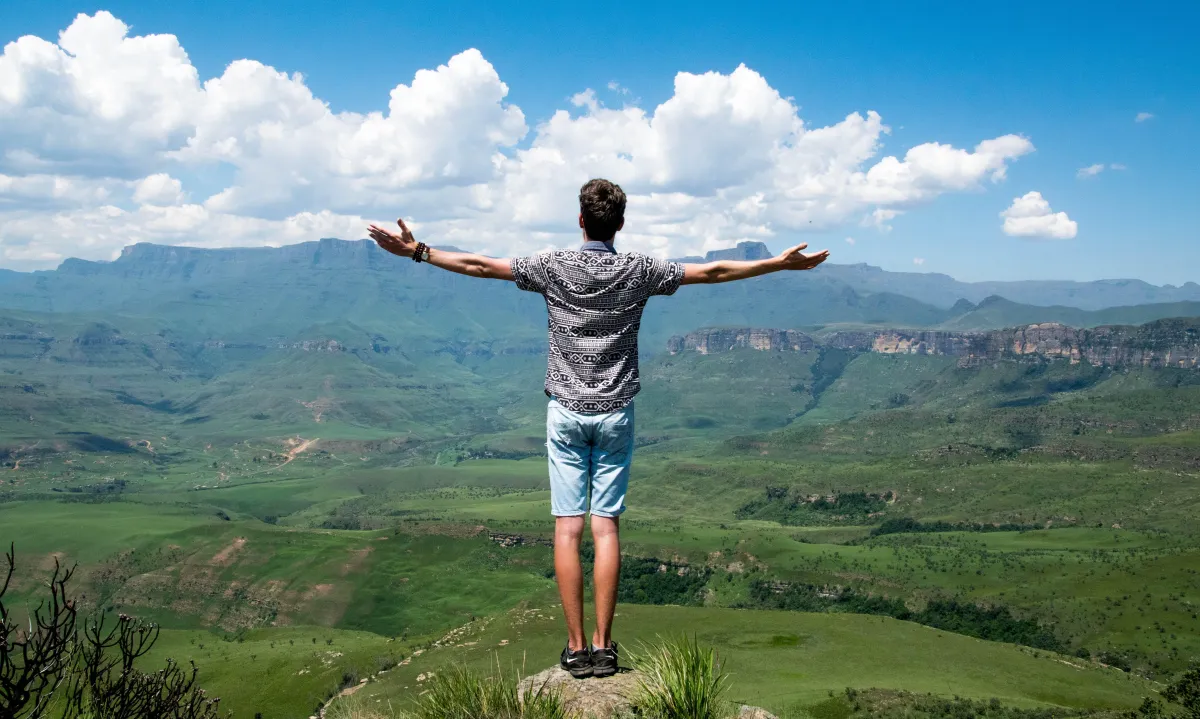 Man standing on mountain holding both arms up taking in the view.