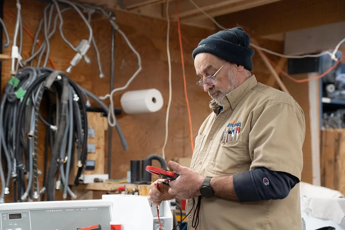 Man using a multimeter to check a washing machine in a workshop.