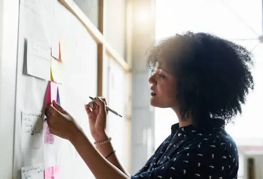 A woman of color writing finding a purpose affirmations on her board
