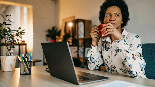 A woman working at a bright desk with indoor plants and a reusable water bottle, showcasing simple, everyday ways to go green in a busy workday.