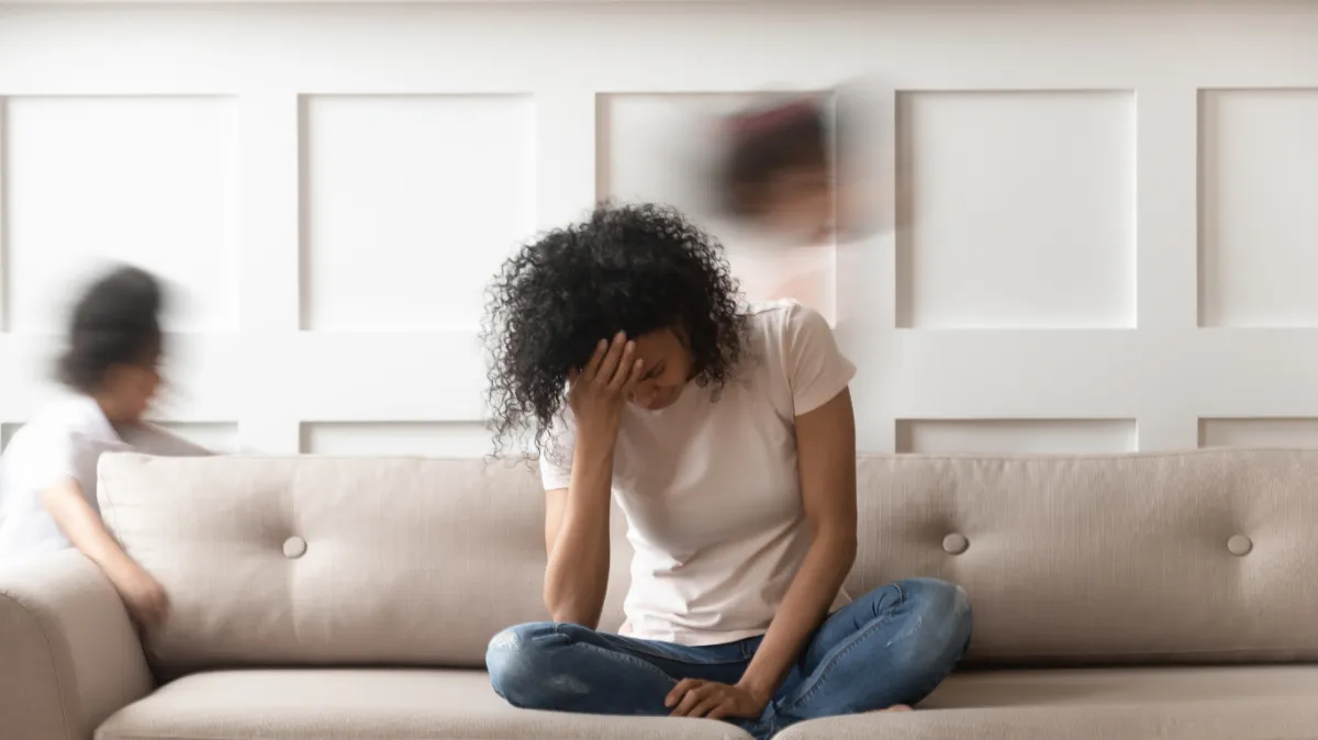 Stressed person sitting on a couch surrounded by blurred children, illustrating overwhelm and exhaustion—key themes in Adrenal Fatigue Signs & How to Recover Naturally