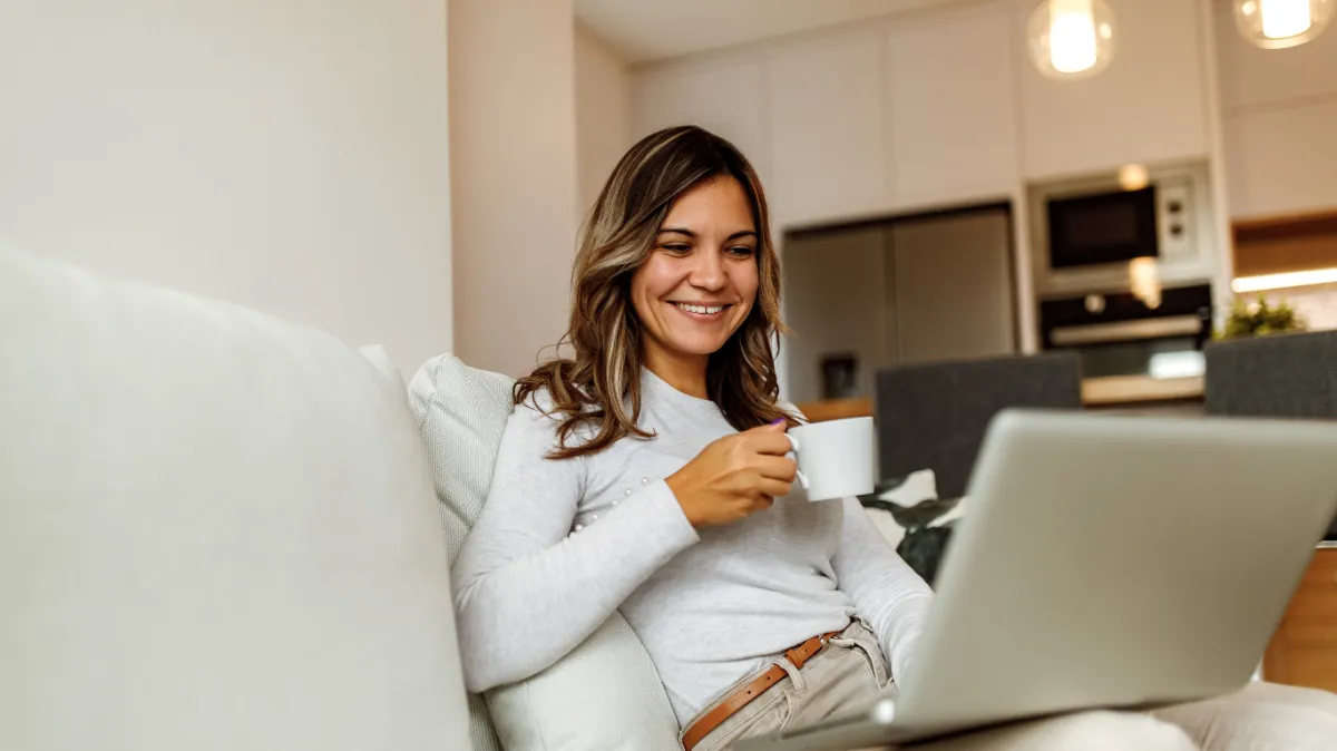 Smiling person enjoying coffee while working on a laptop in a bright kitchen, reflecting a calm and focused Morning Routine for Productivity: Align Your Mind and Body