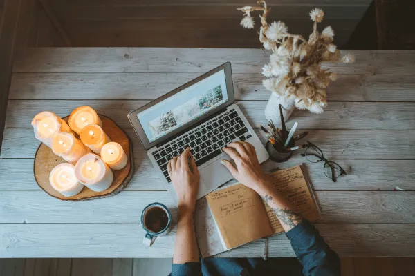 Hände einer Frau am Laptop, Kerzen und Strohblumen auf dem Tisch