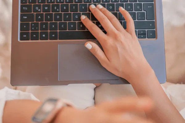 brauner Laptop, eine Frauenhand schreibt