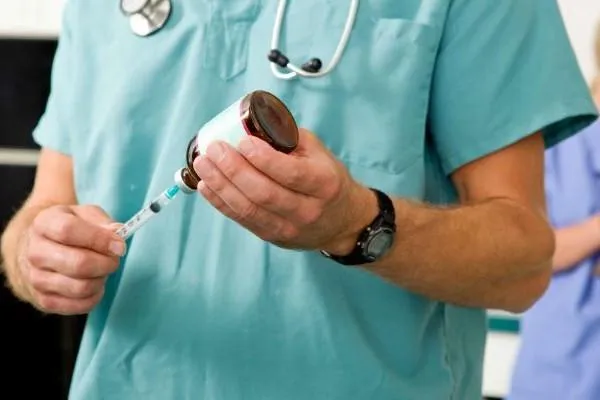 person in vet scrubs with bottle and syringe