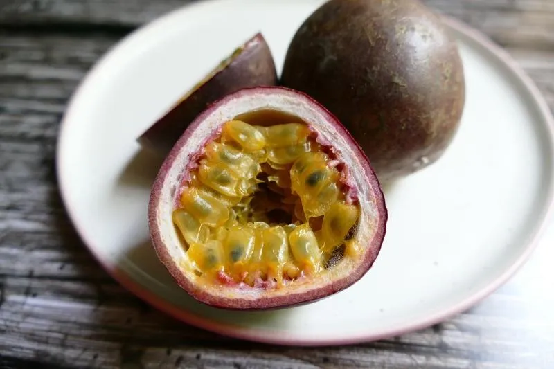 two passionfruit, one sliced, on a white plate