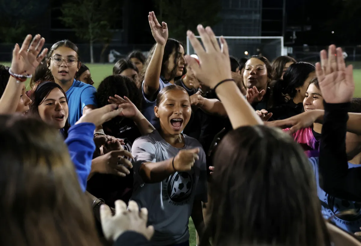A diverse group of young immigrant soccer players in Boston celebrating a goal together on a neighborhood field