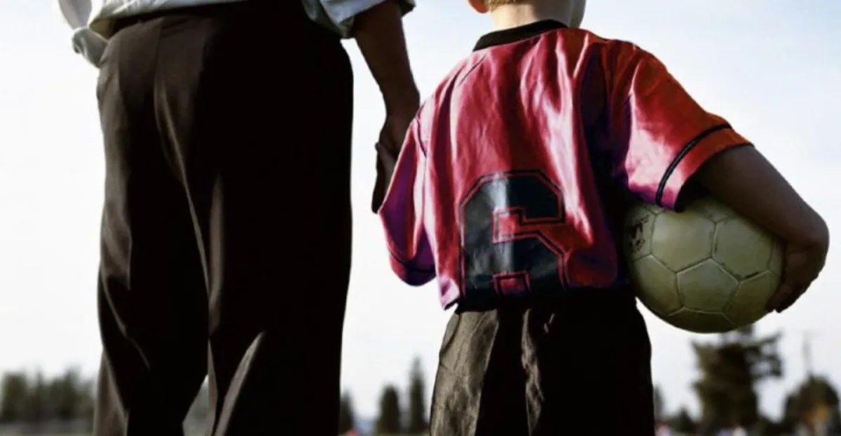 A calm parent clapping supportively on the sidelines while youth soccer players listen to their coach during a game in Massachusetts