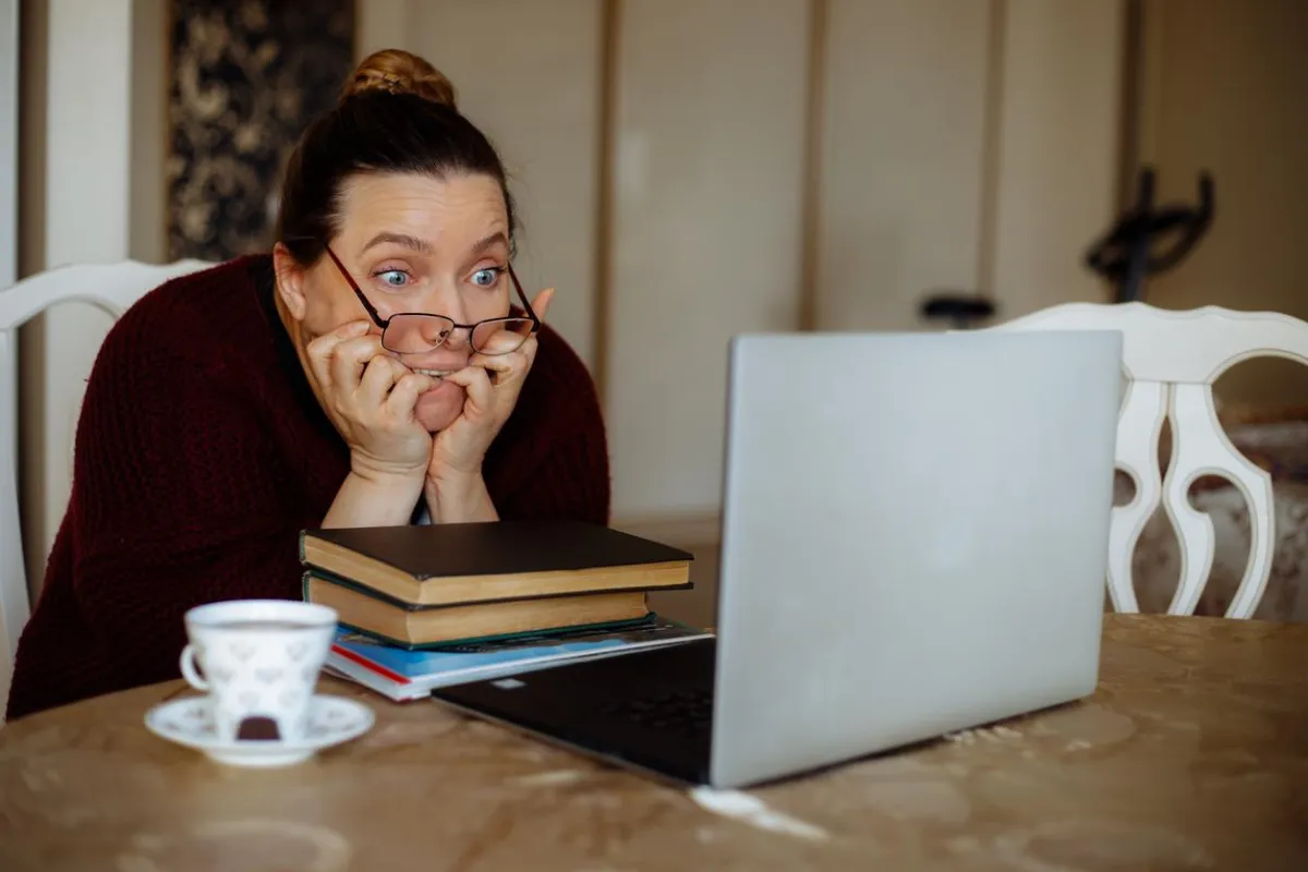 scared middle-aged woman sitting at table, looking at laptop overwhelmed by all the Steps of Buying and Selling her Home