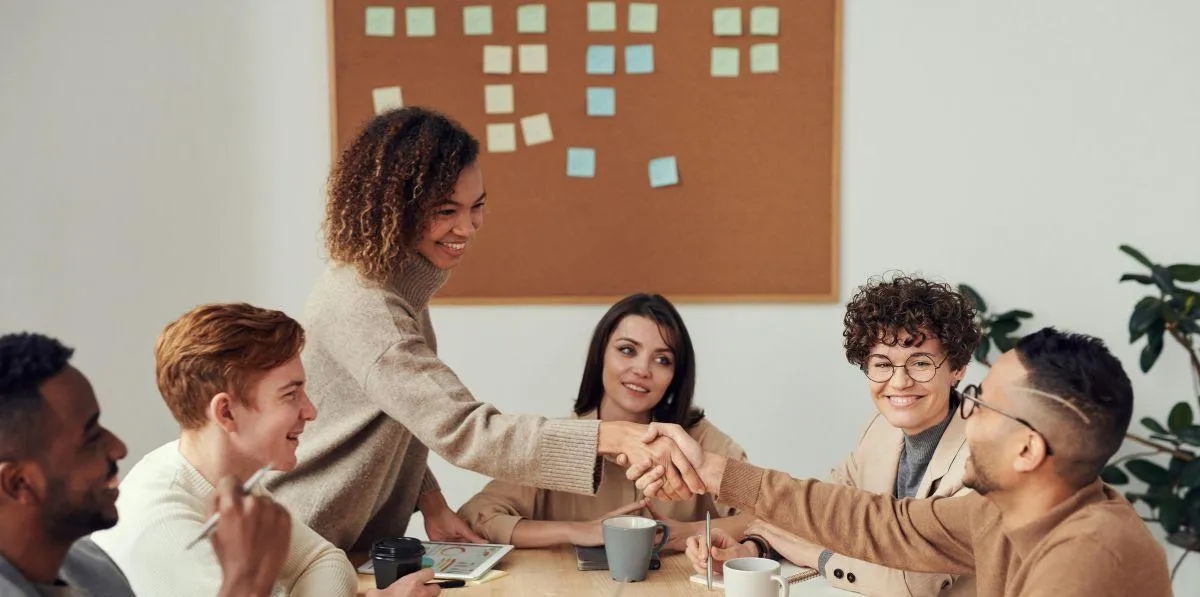 Colleagues in a meeting smiling and shaking hands at a table.