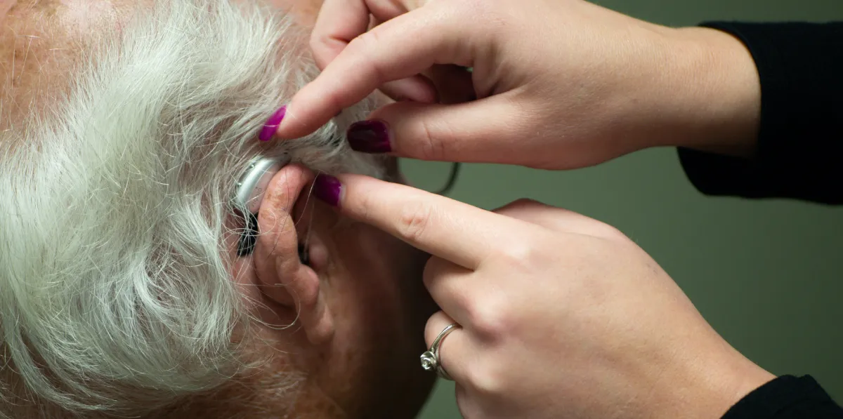 Person assisting an elderly individual with a hearing aid.