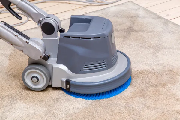 Close-up of a professional carpet cleaning machine with a rotating blue brush cleaning a carpet