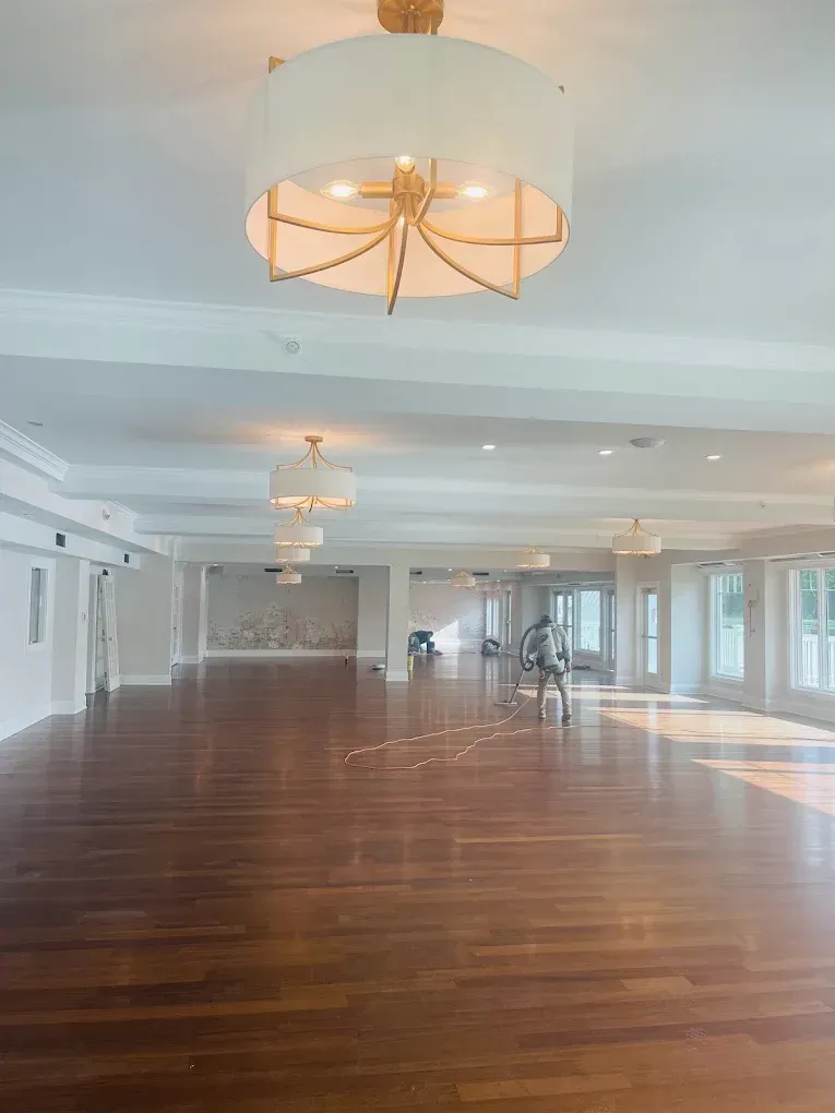 Interior space with wooden flooring and modern lighting fixtures, featuring a painter using a spray machine, representing Victory Painting's professional painting services.