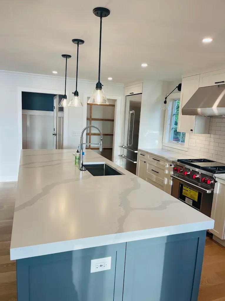 Modern kitchen interior featuring a large island with a light-colored countertop, stainless steel appliances, black pendant lighting, and a stylish sink, showcasing high-quality craftsmanship by Victory Painting LLC.