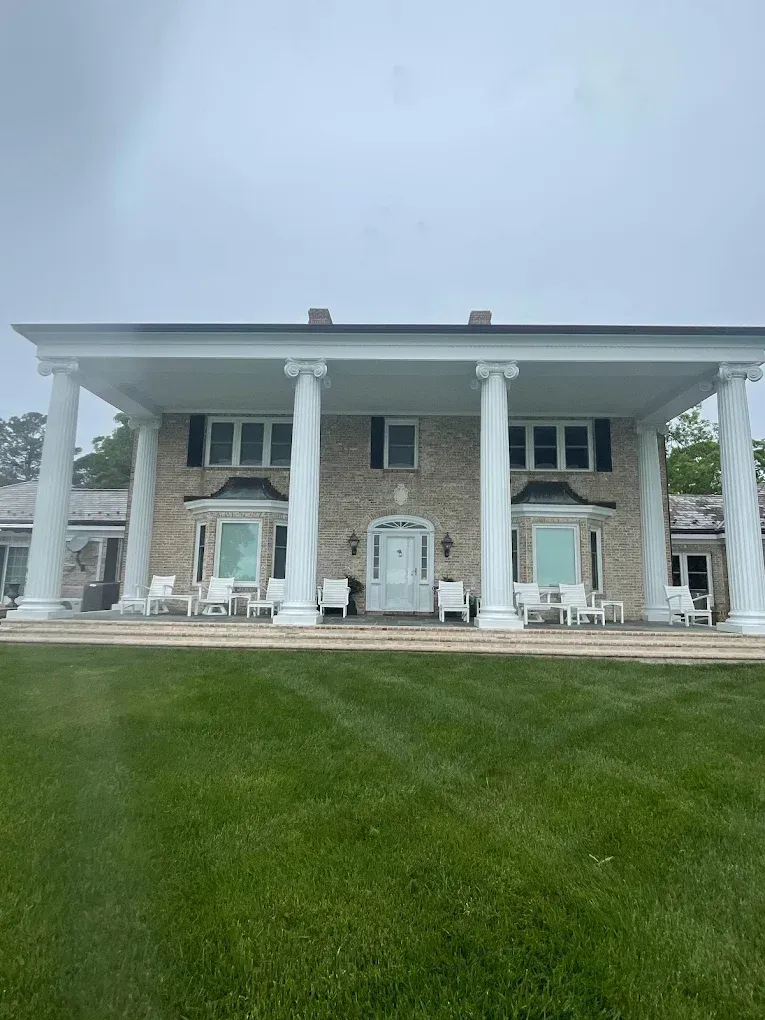 Elegant two-story house with large columns, front porch seating, and manicured lawn, showcasing professional exterior painting by Victory Painting in Easton, MD.