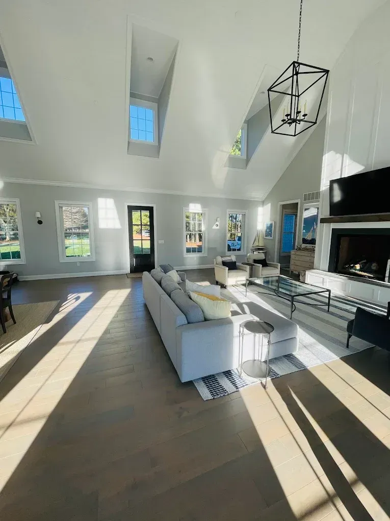 Bright and airy living room showcasing modern design with large windows, vaulted ceiling, stylish furniture, and natural light, reflecting high-quality interior painting by Victory Painting LLC.