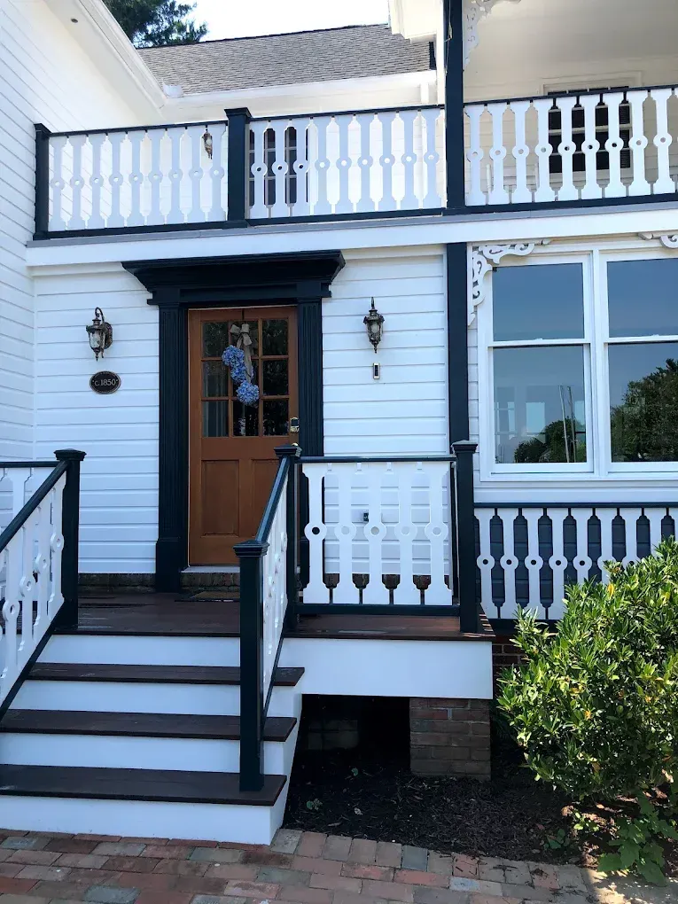 Victorian-style home entrance with wooden door, decorative porch railings, and landscaped greenery, showcasing high-quality residential painting by Victory Painting LLC in Easton, MD.