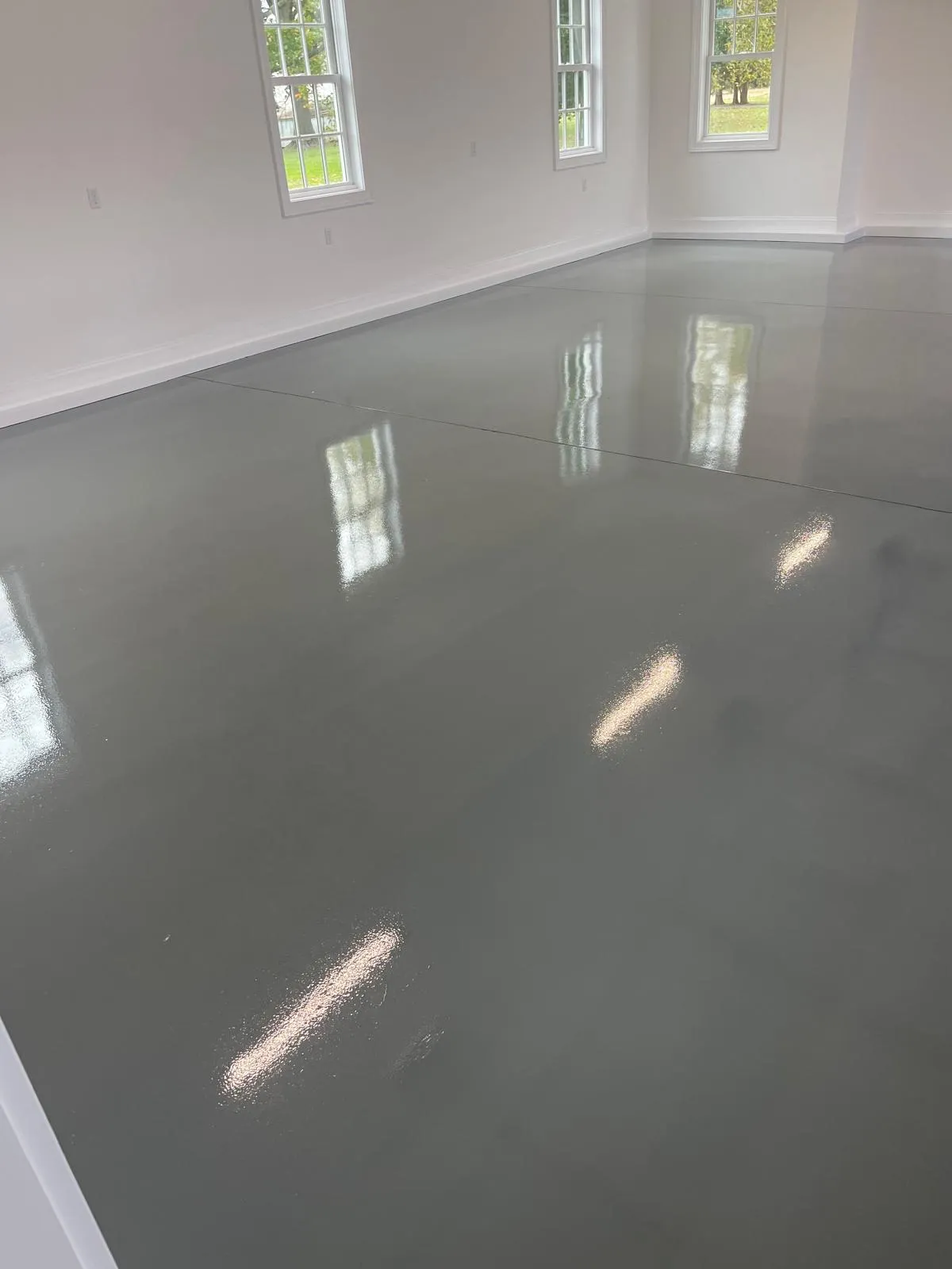 Freshly painted gray interior floor with reflections, in a well-lit room featuring white walls and windows, showcasing the quality craftsmanship of Victory Painting LLC in Easton, MD.