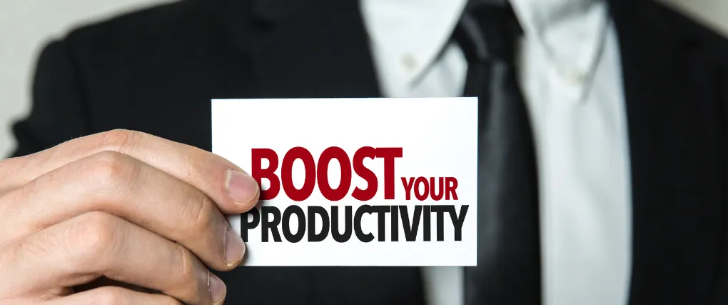 A professional man in a black suit holding a business card that reads 'BOOST YOUR PRODUCTIVITY' in bold red letters. The background is intentionally blurred to focus on the card and the text, highlighting a motivational and business-oriented theme.