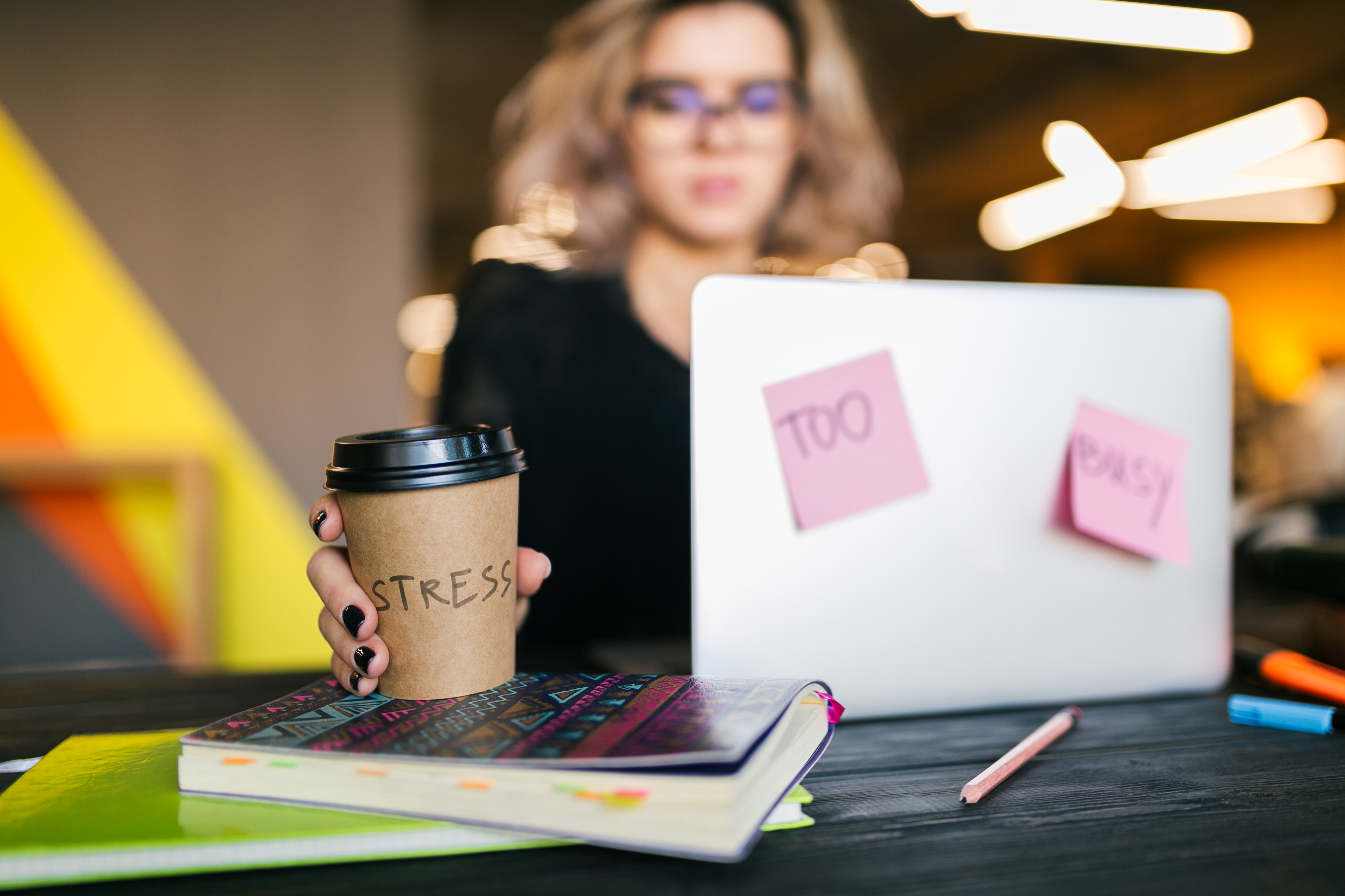 Woman at her laptop with a coffee cup that says stress and sticky notes that say too busy.