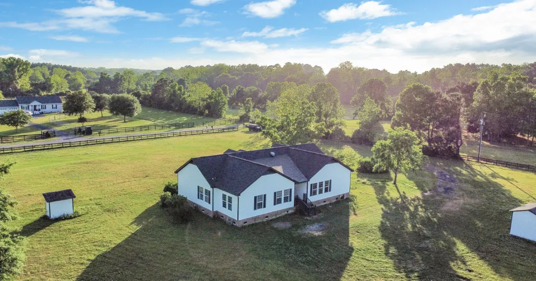 Aerial view of a white country house on green acreage in rural Oklahoma with trees and open land