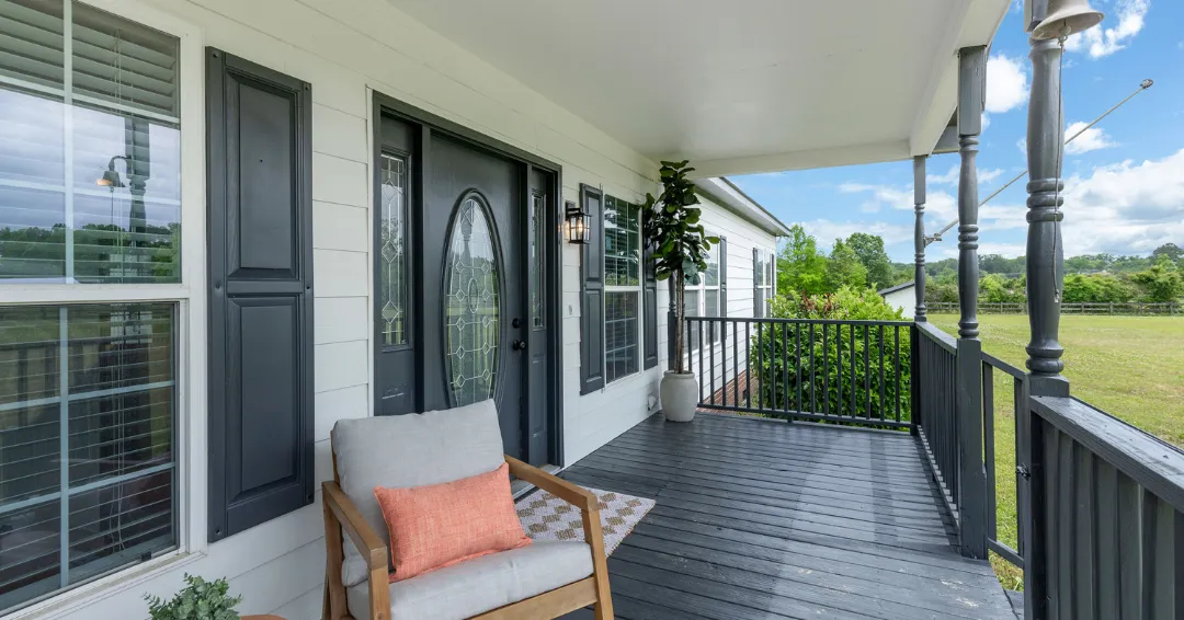 Beautiful front porch of a country home with black shutters, a cozy sitting area, and scenic outdoor views.
