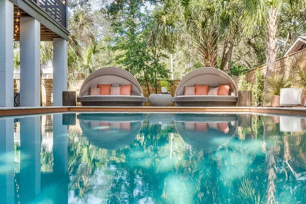 Outdoor pool area with twin luxury daybeds, tropical trees, and modern landscaping in Oklahoma home