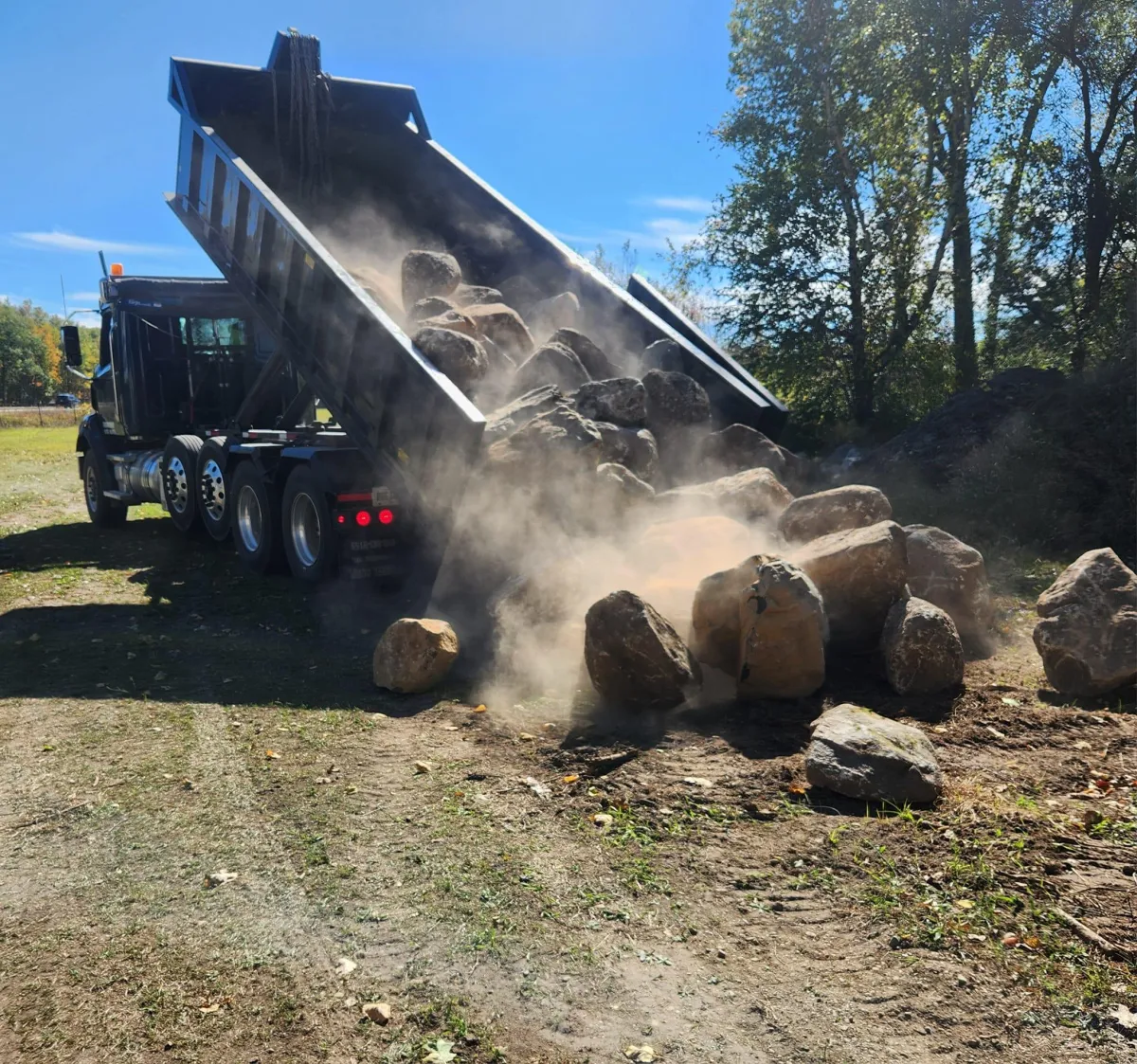 A truck dropping off a supply of boulder for a boulder wall hardscape project