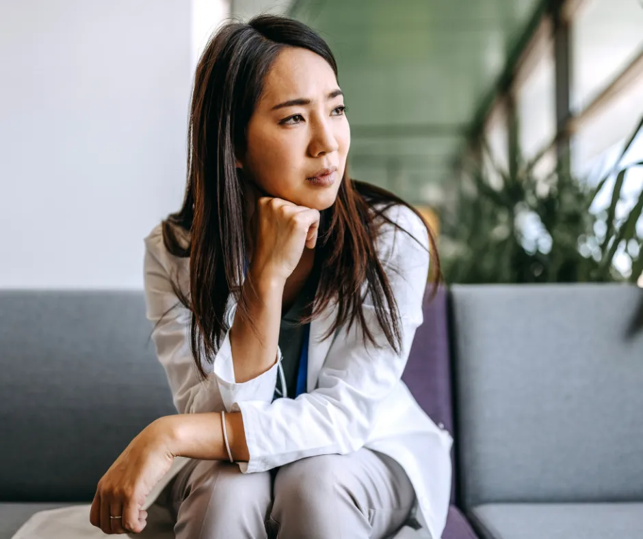 A thoughtful woman sitting on a couch, resting her chin on her hand, gazing into the distance with a pensive expression, symbolizing self-reflection and introspection.