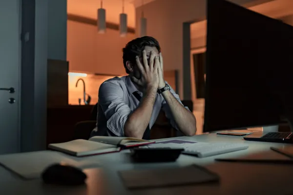 A tired professional sitting at a desk with their head resting on their arms, symbolizing emotional burnout.
