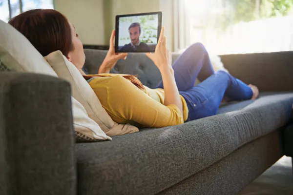 A happy couple on a couch, smiling and talking openly with each other through a tablet.