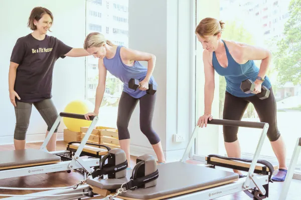 Women doing dumbbell rows while supporting body on footbar of reformer