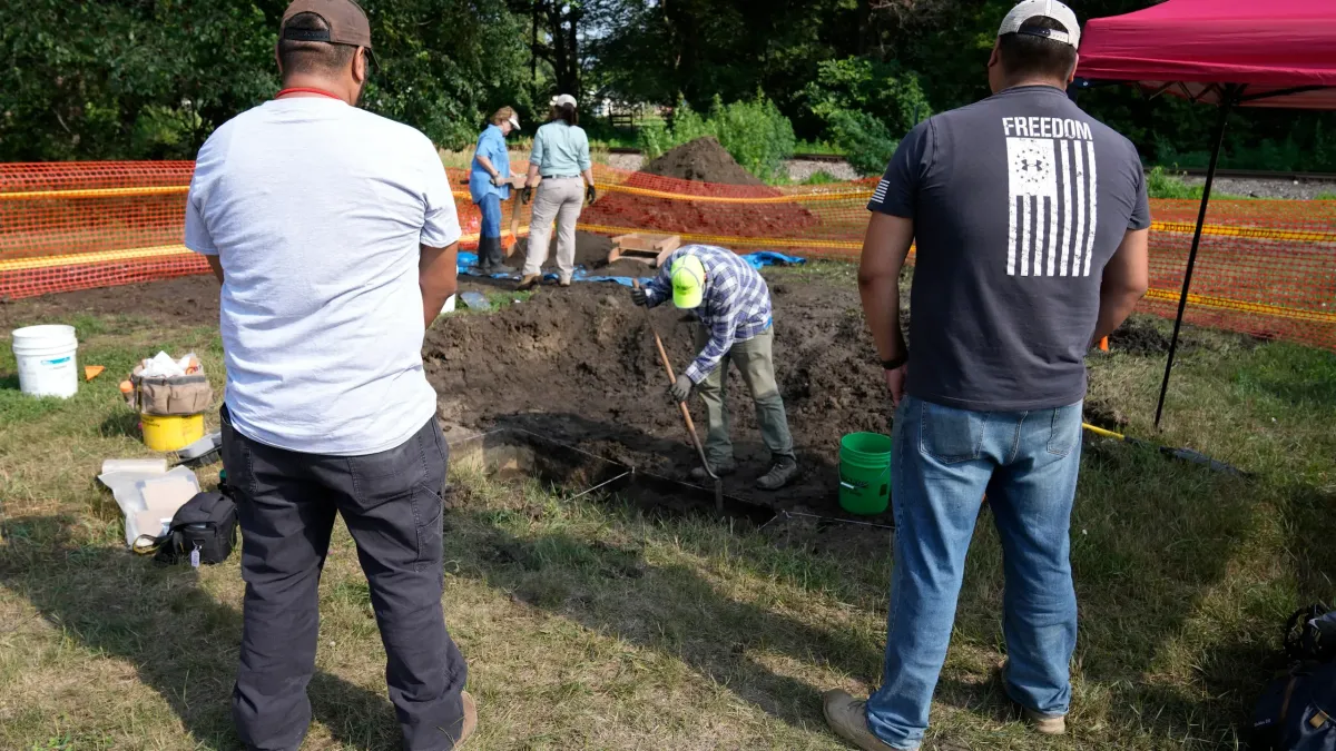 Omaha Tribe members Mark Parker, left, and Jarell Grant, both of Macy, Neb., watch as workers dig for the suspected remains of children who once attended the Genoa Indian Industrial School,
