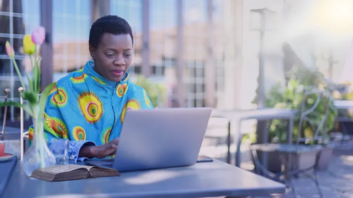 A confident Christian woman working on her laptop with a Bible open beside her, exuding clarity, purpose, and faith-driven focus in her digital journey.