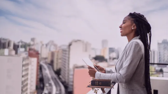 Confident Christian woman standing with a Bible and laptop, symbolizing clarity, purpose, and stepping into a new level of impact.