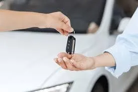 customer handing over car keys to a dealer with a trade-in vehicle in the background.