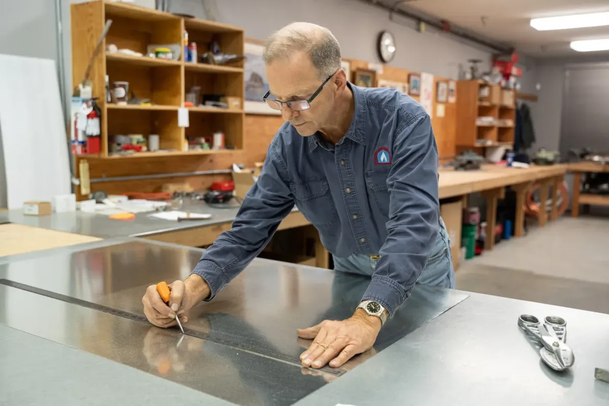 Technician measuring and marking sheet metal in a Vancouver workshop, preparing HVAC and gas heating components for fall system maintenance — Superior Gas Installations & Service Ltd.