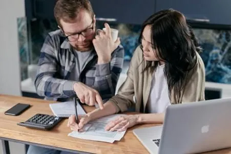 man and woman reviewing debt with paper and computer